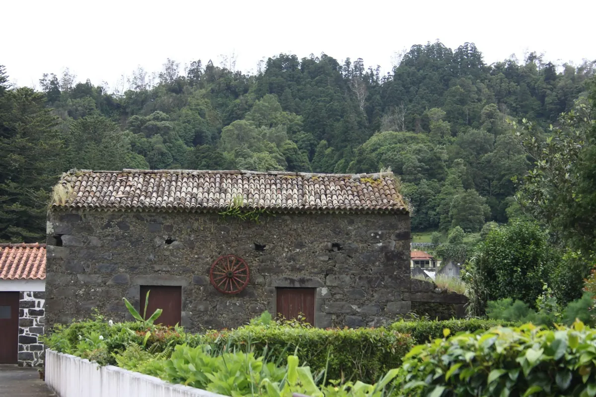 A single-storey house of dark volcanic stone with a clay tile roof and two timber doors, set in a green garden